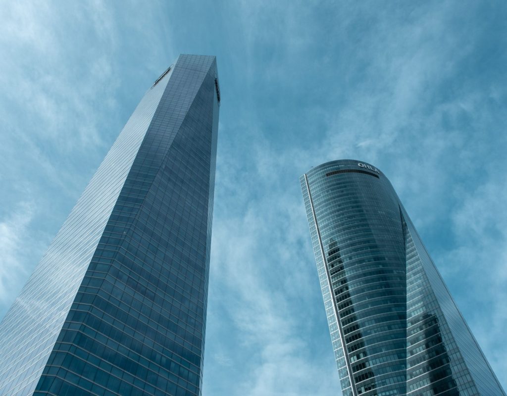A low-angle view of two modern skyscrapers in Madrid, Spain against a clear blue sky.