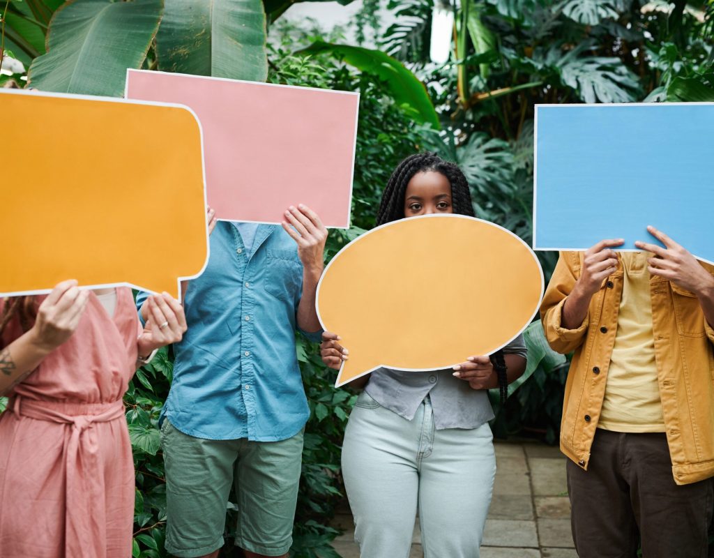 A group of adults holding colorful speech bubble signs in a lush greenhouse setting.